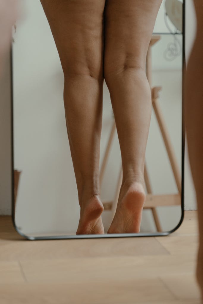 Artistic reflection of a woman's legs in a mirror, emphasizing natural beauty and self-awareness.