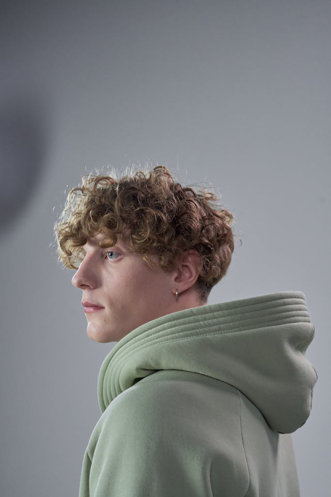 Portrait of a man with curly hair wearing a green hoodie, captured in a studio setting.