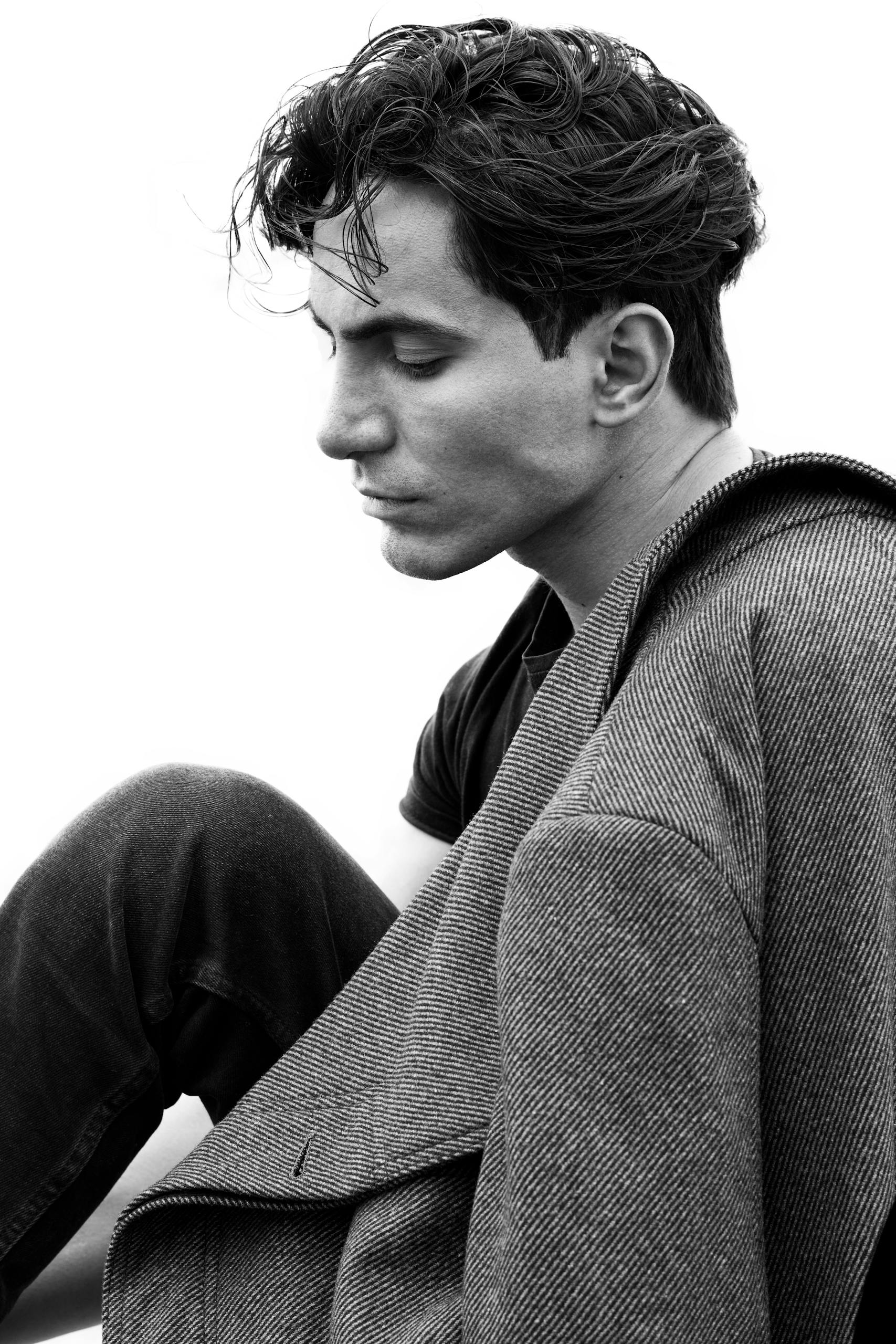 Stylish black and white portrait of a young man in a coat and casual attire, exuding elegance.