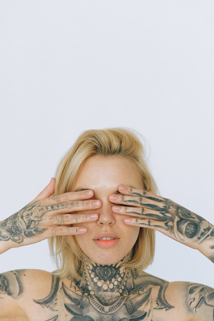 Donna bionda con tatuaggi visibili che copre gli occhi con le mani, simbolo di consapevolezza e cambiamento legato alla rimozione tatuaggi Torino.